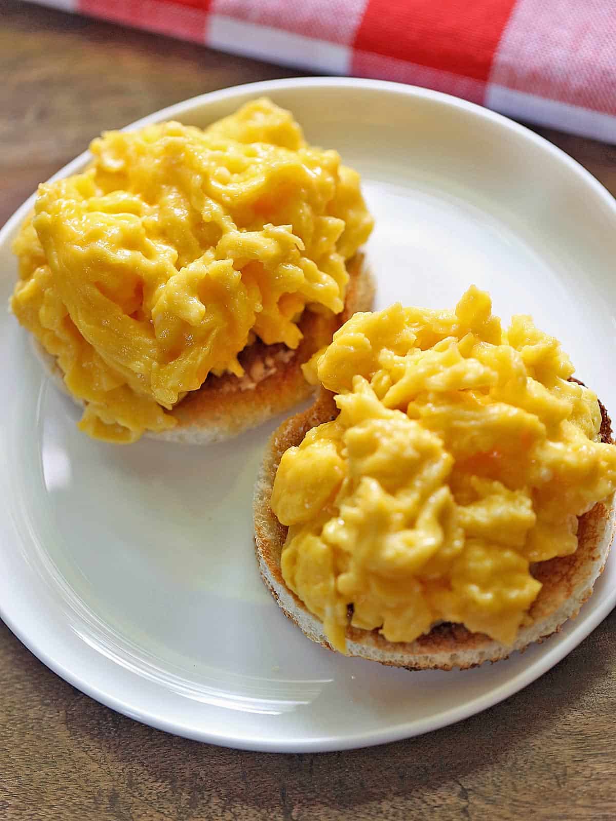 Soft scrambled eggs are served on an English muffin.