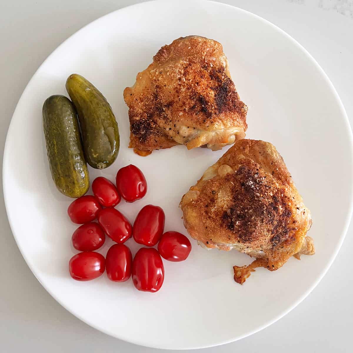 Crispy baked chicken thighs are served with cherry tomatoes and dill pickles.
