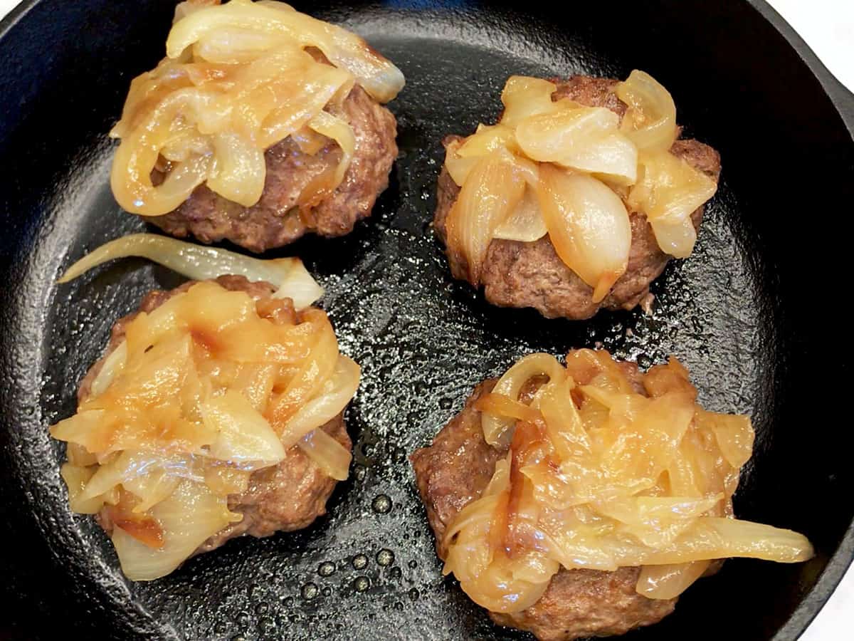 Four burgers are topped with sauteed onions.