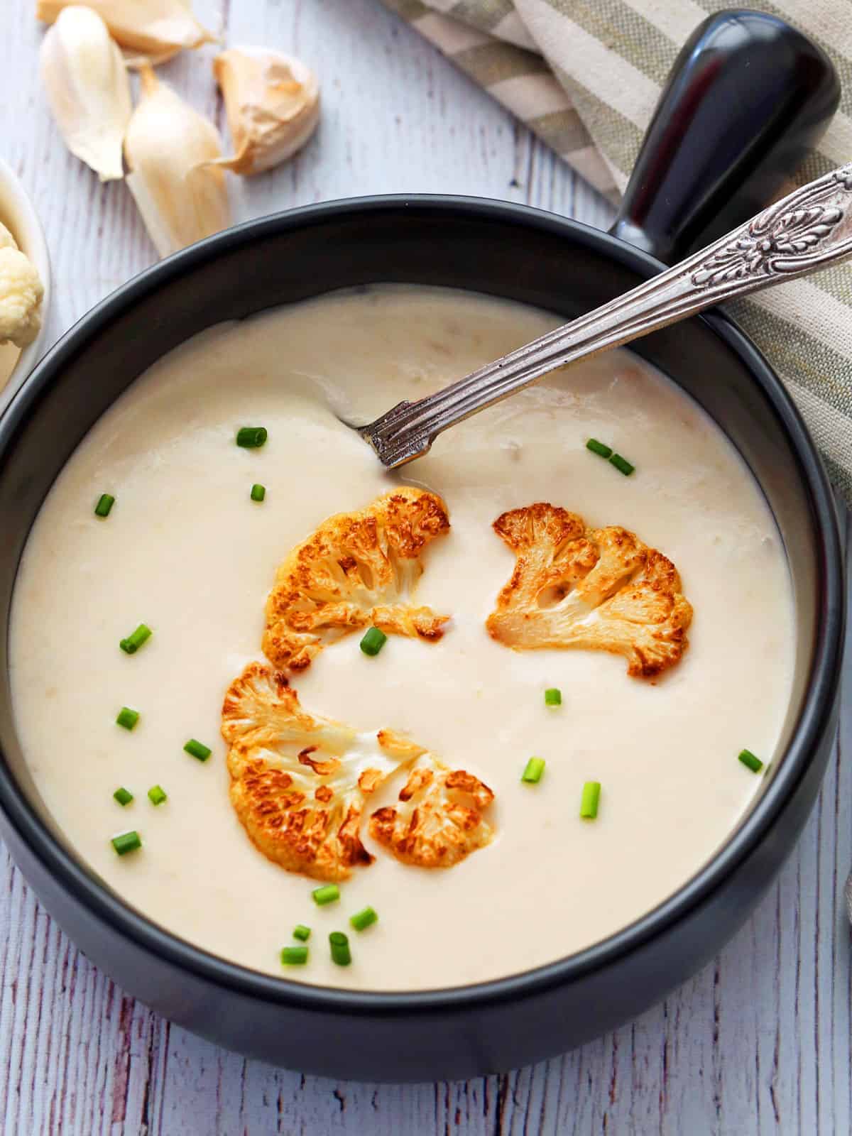 Cream of cauliflower soup is served in a black soup bowl, garnished with cauliflower florets.