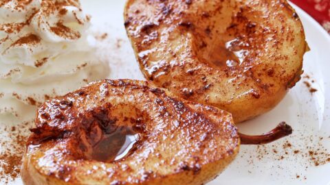 Baked pears are served on a white plate with whipped cream.