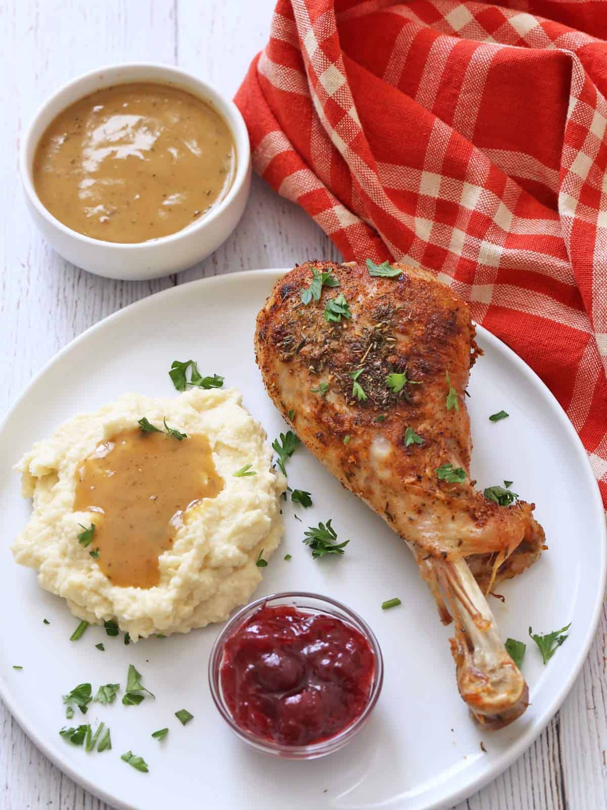 Mashed cauliflower is topped with gravy and served with a turkey leg and cranberry sauce.