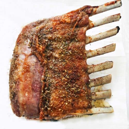 A roasted rack of lamb on a parchment-lined baking sheet.
