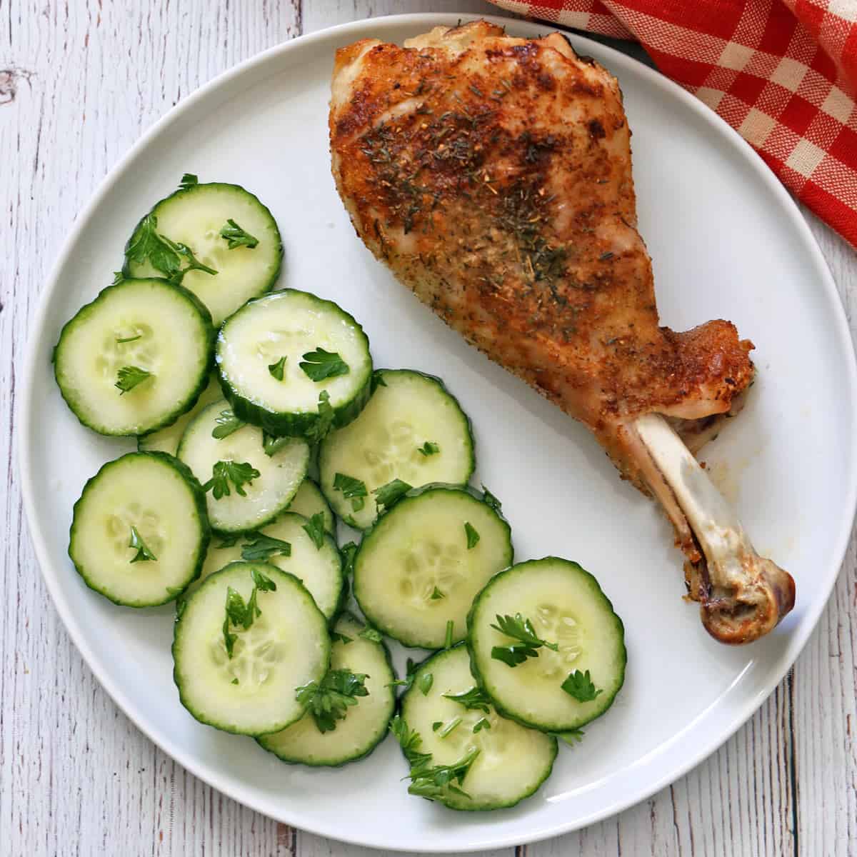 Cucumber vinegar salad is served as a side dish to a roasted turkey leg.