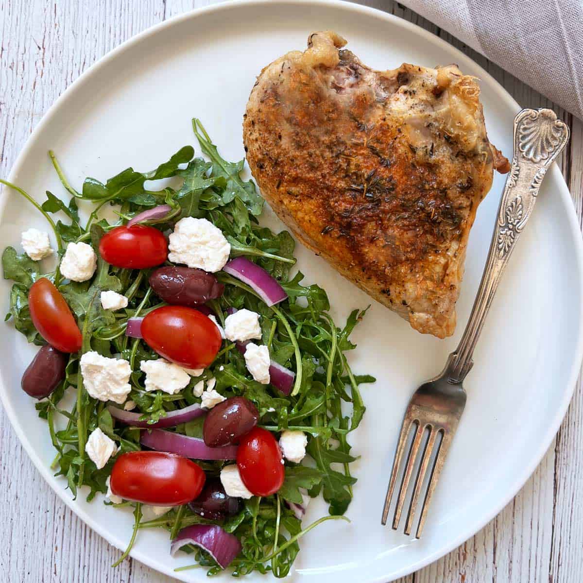 Arugula salad is served with bone-in, skin-on chicken breast.