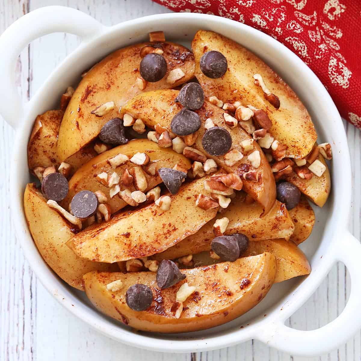 Baked apple slices are topped with chopped nuts and chocolate chips.
