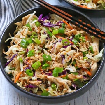 Chinese chicken salad is served in a dark bowl with chopsticks.