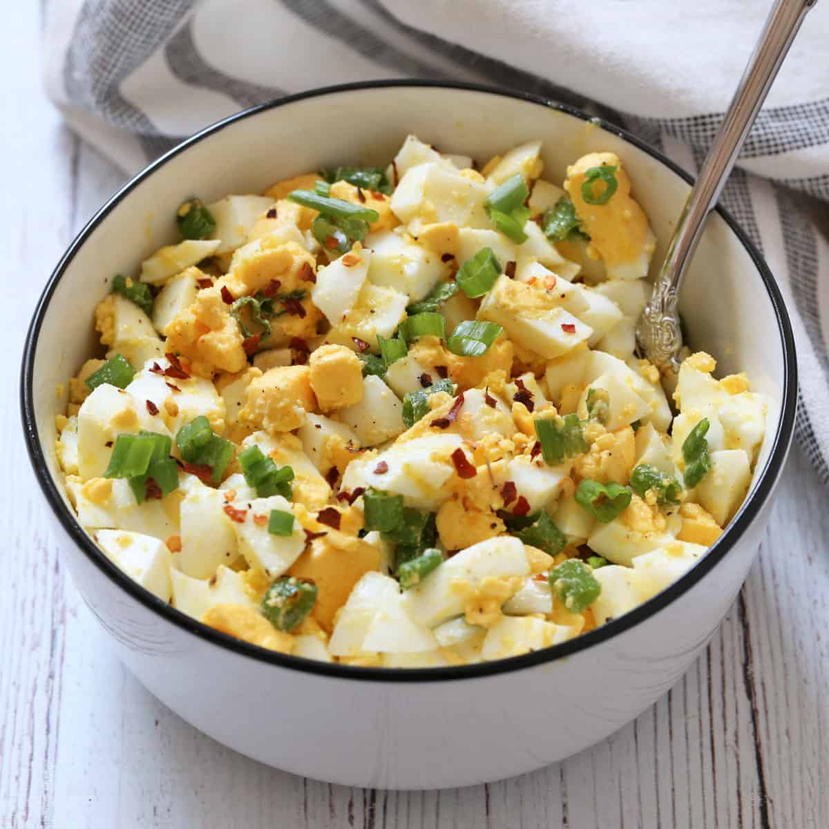Olive oil egg salad with scallions is served in a bowl with a spoon.