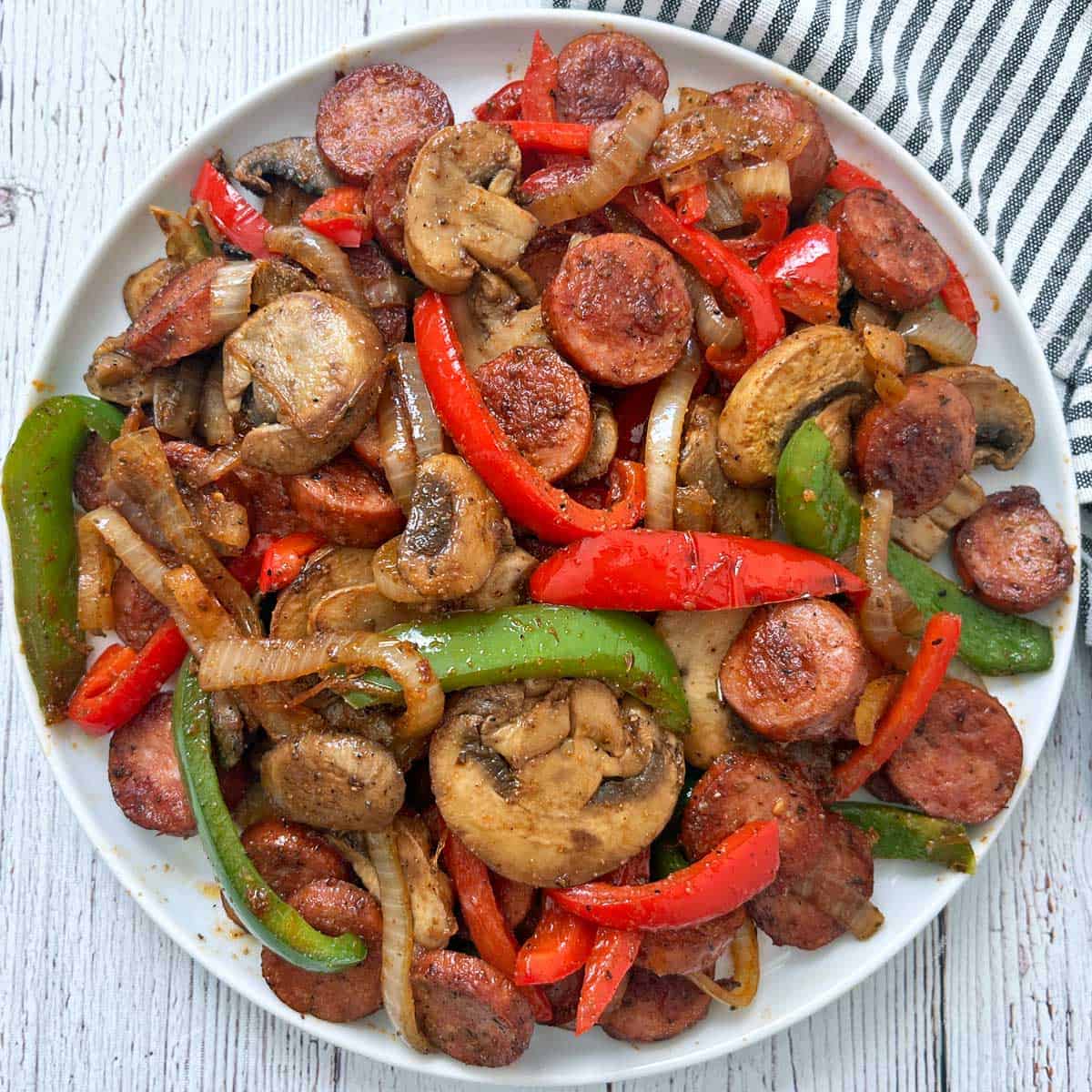 Sausage and peppers with added mushrooms on a white plate.