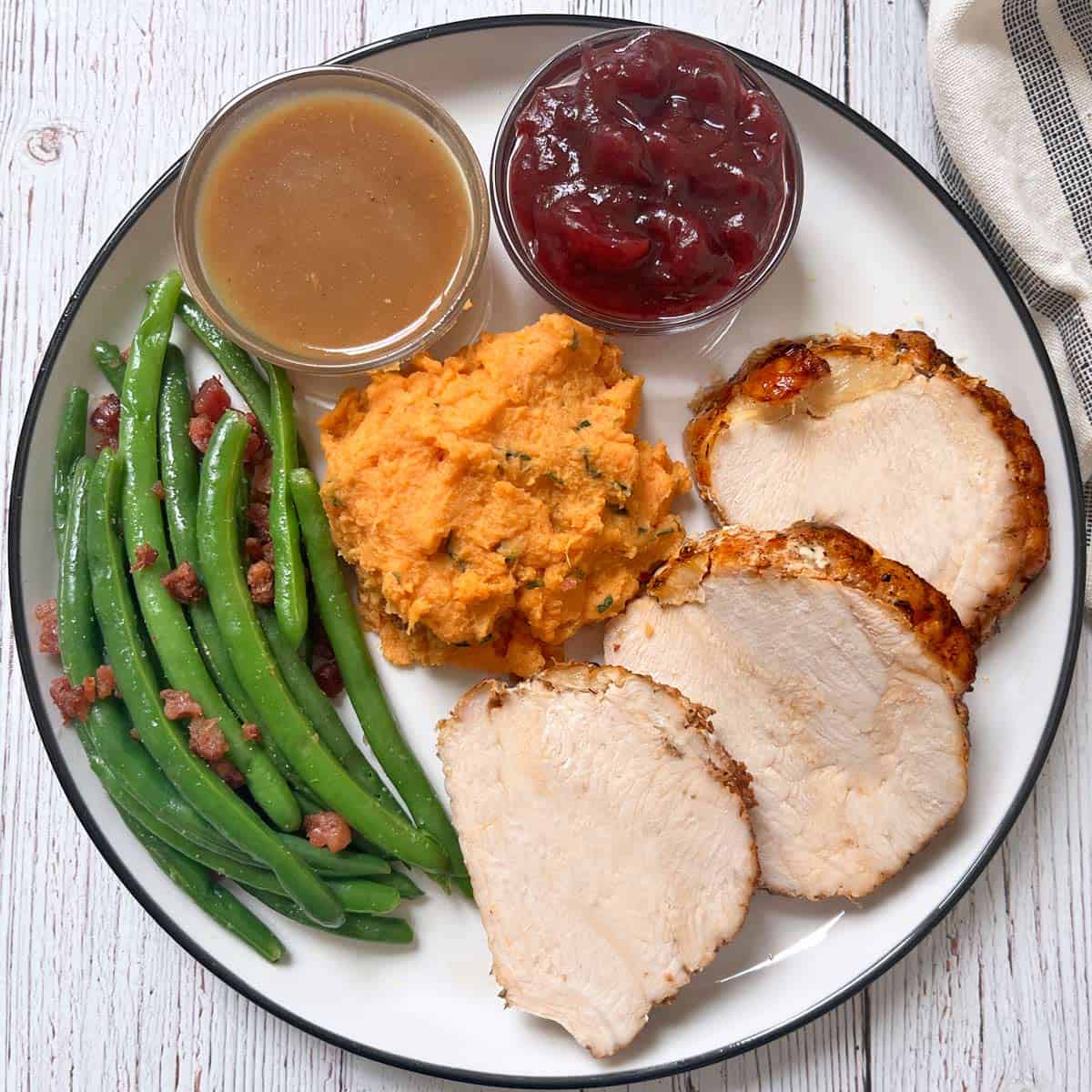 A Thanksgiving plate with turkey breast, mashed sweet potatoes, green beans with bacon, cranberry sauce, and gravy.