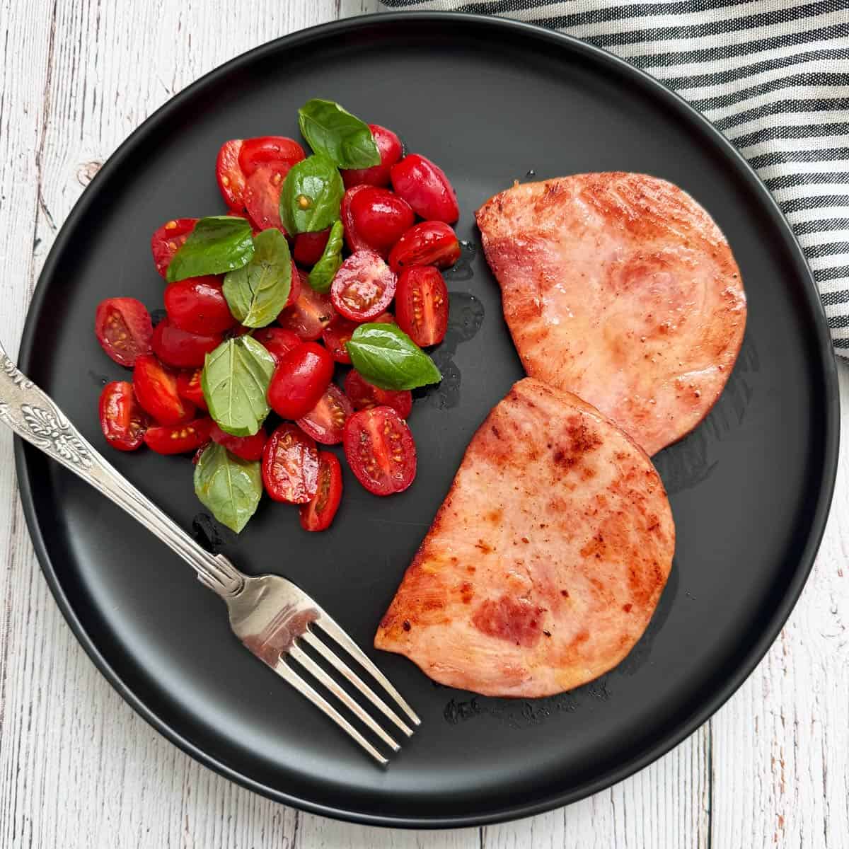 Tomato salad with basil instead of scallions is served with ham steak.