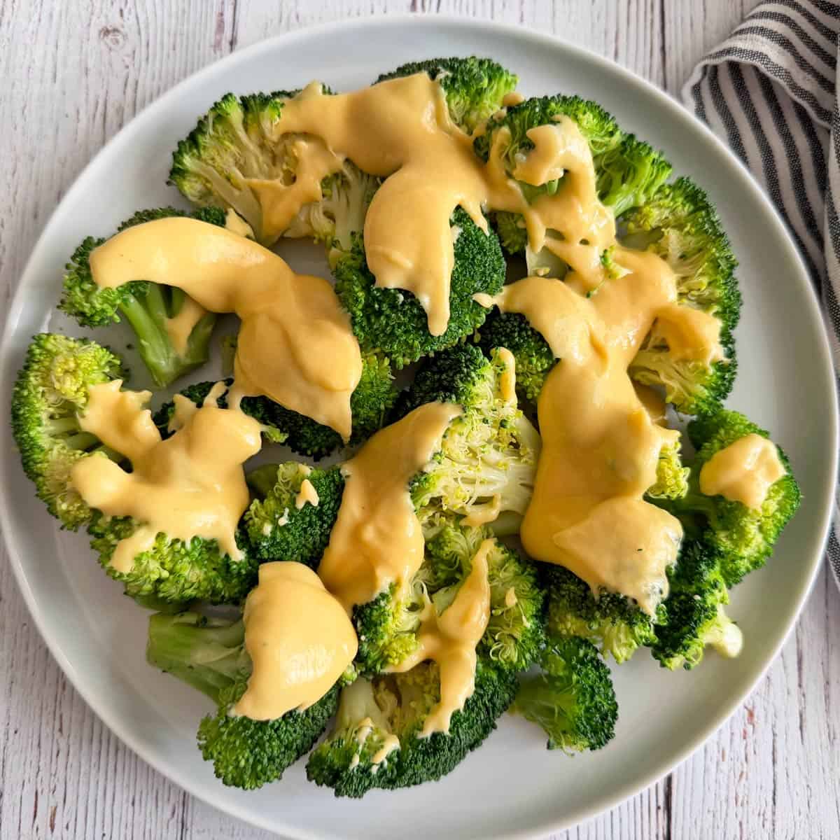 Broccoli is topped with a thick cheese sauce and served on a white plate.