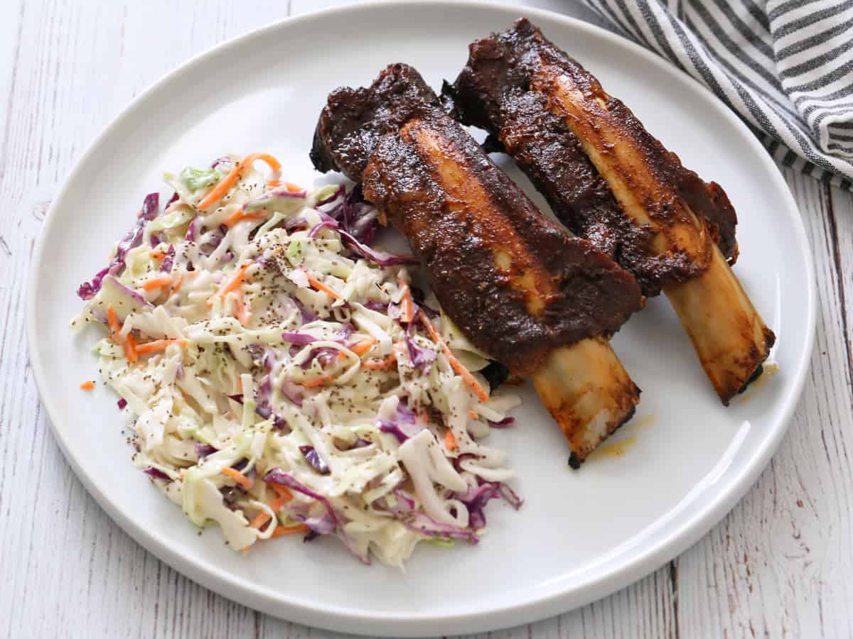 Two beef back ribs are served with a side of coleslaw.