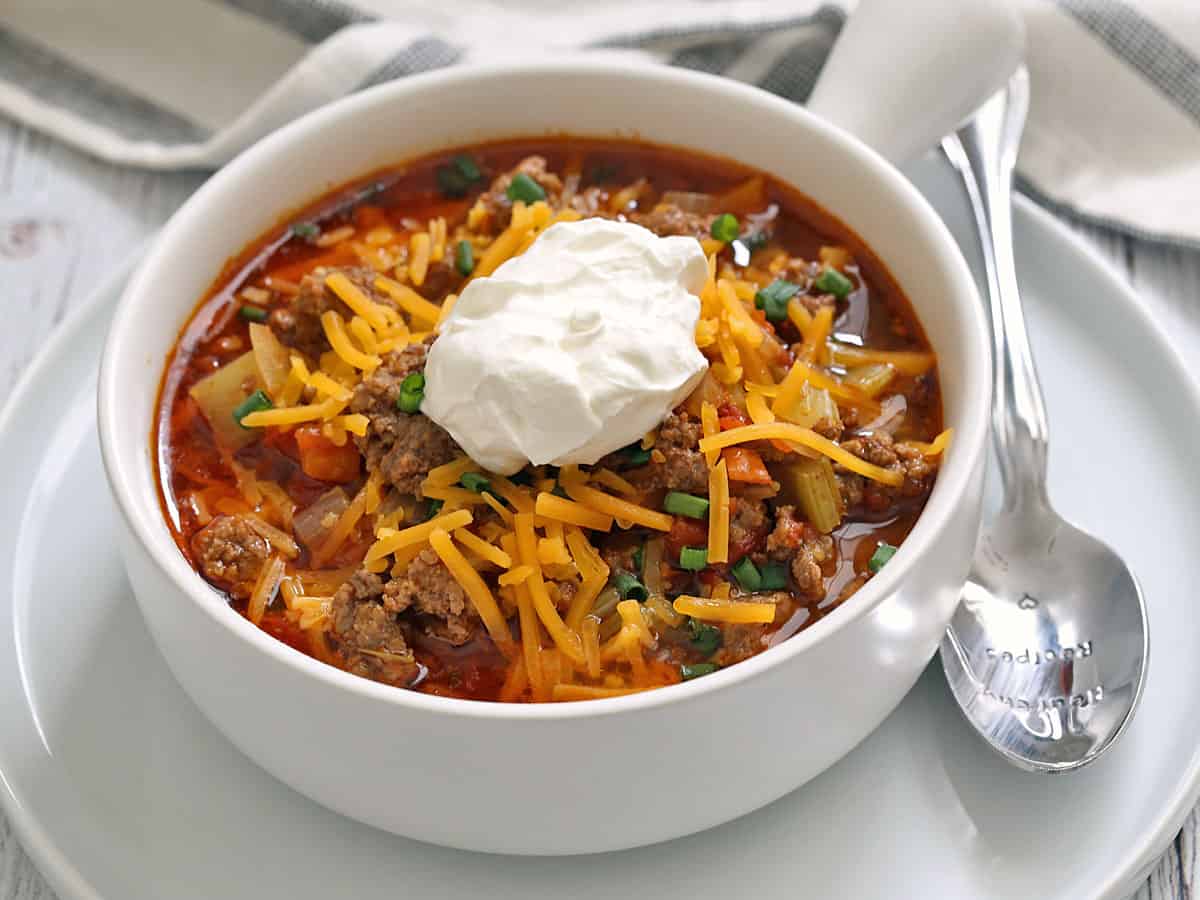Hamburger soup is topped with shredded cheese and sour cream.