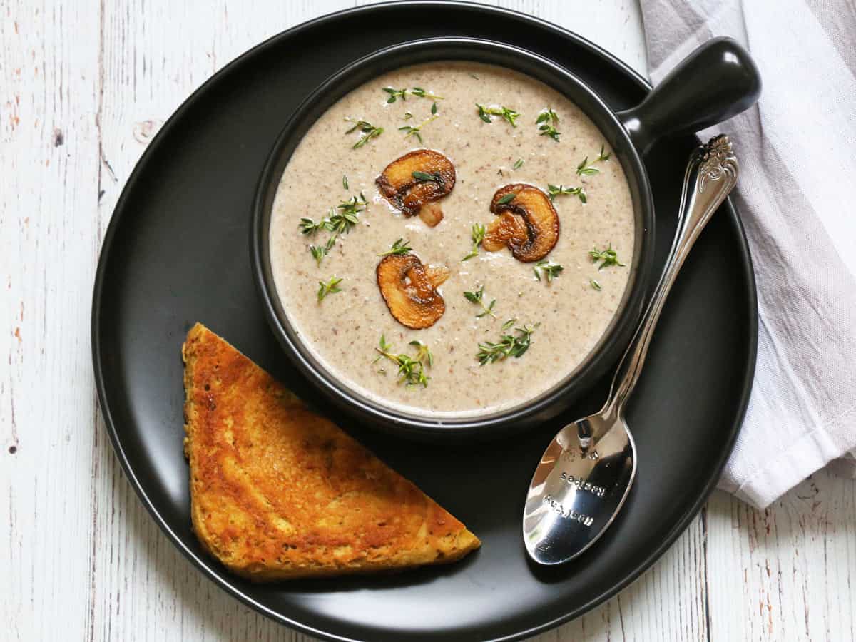 Mushroom soup is served in a dark bowl with a spoon and toast.