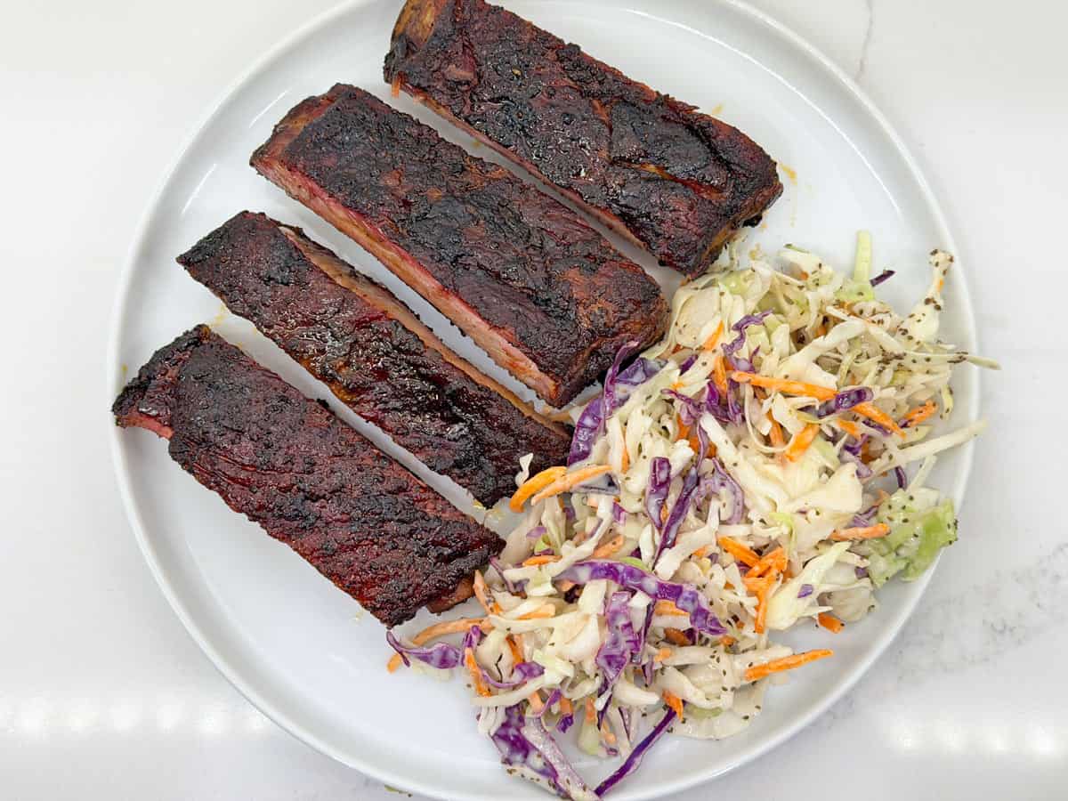 Four pork ribs are served with a side of coleslaw.