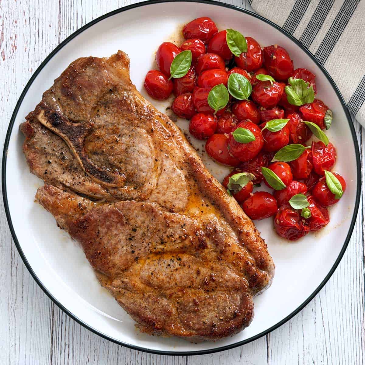 A pork steak is served with roasted tomatoes.