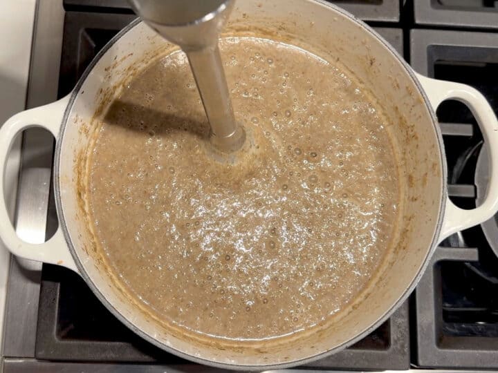 Pureeing the soup using an immersion blender.