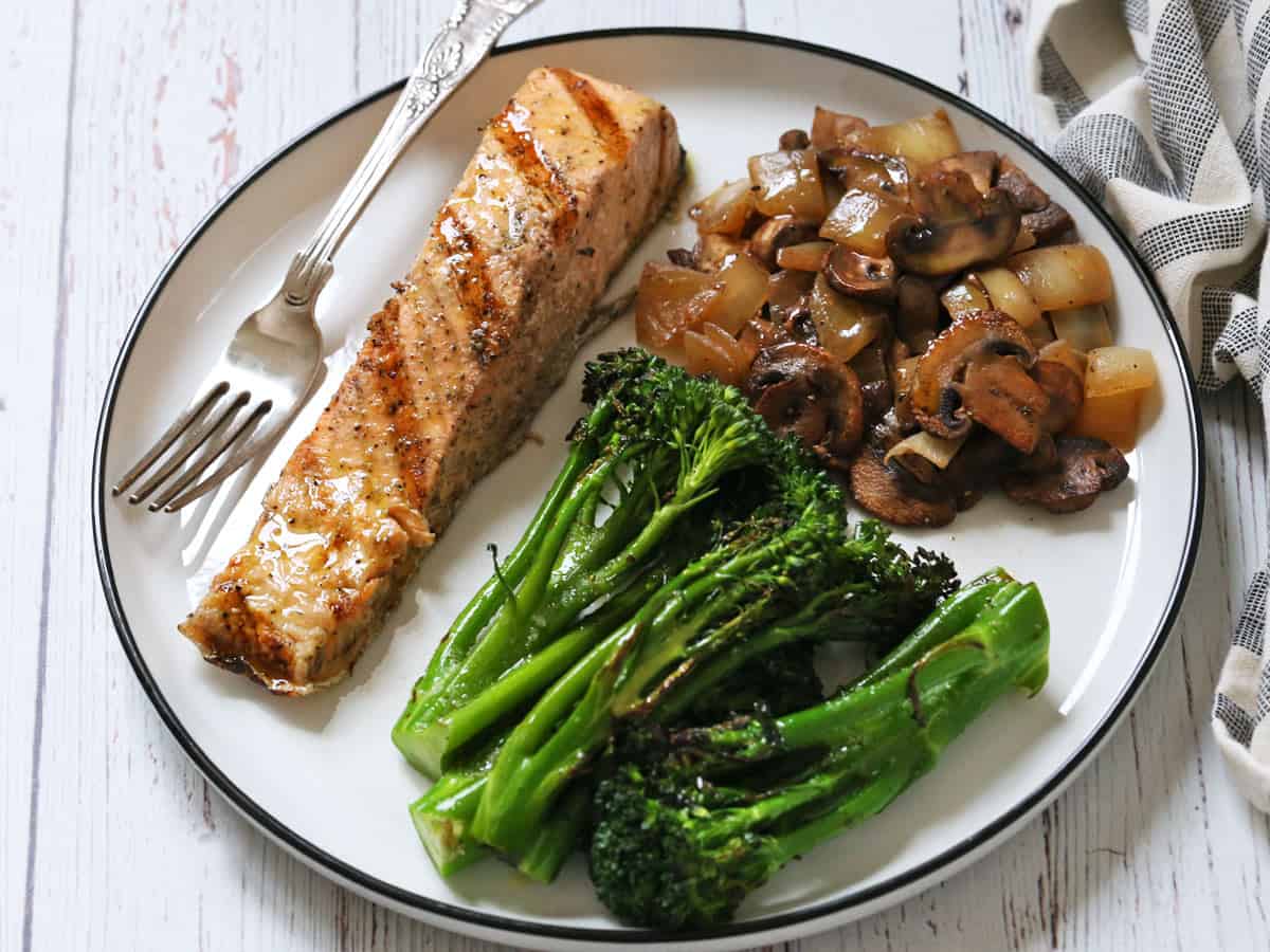 Grilled broccolini is served with salmon and mushrooms.
