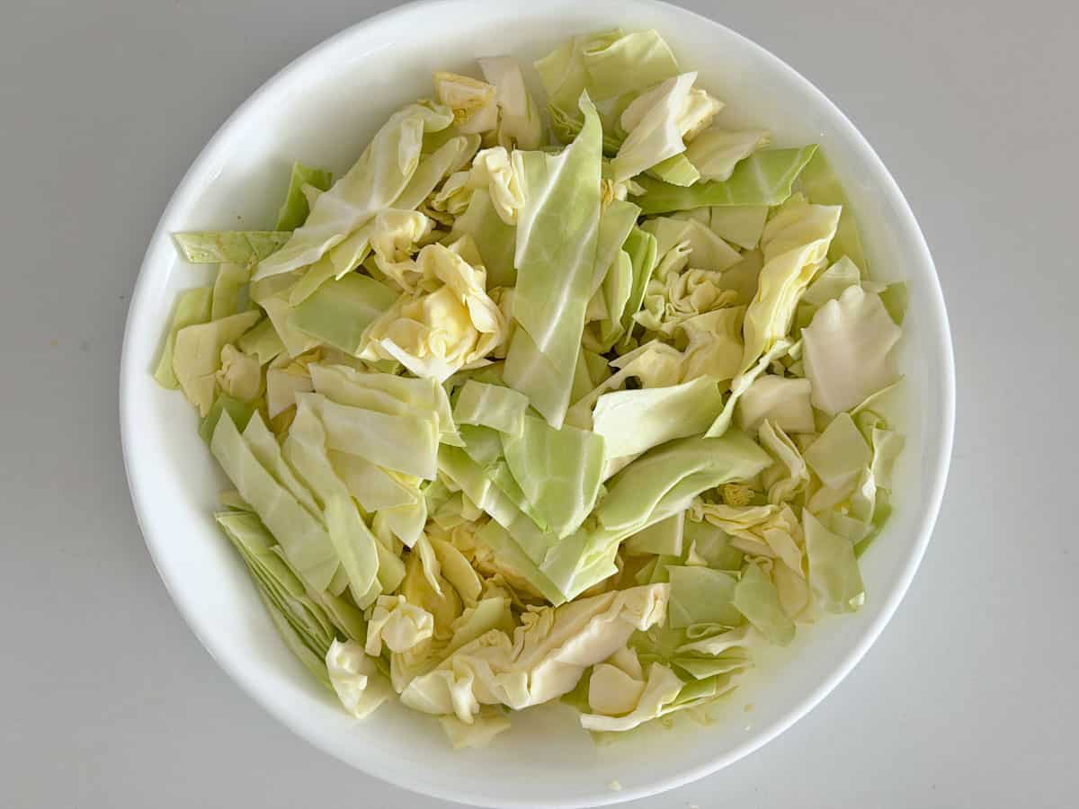 A coarsely shredded cabbage in a white bowl.