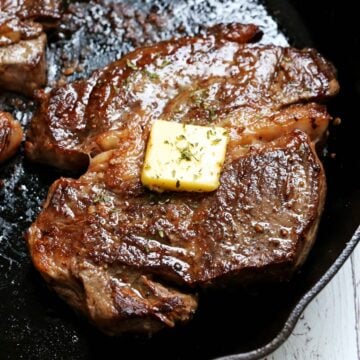 A chuck eye steak in a cast-iron skillet is topped with butter.