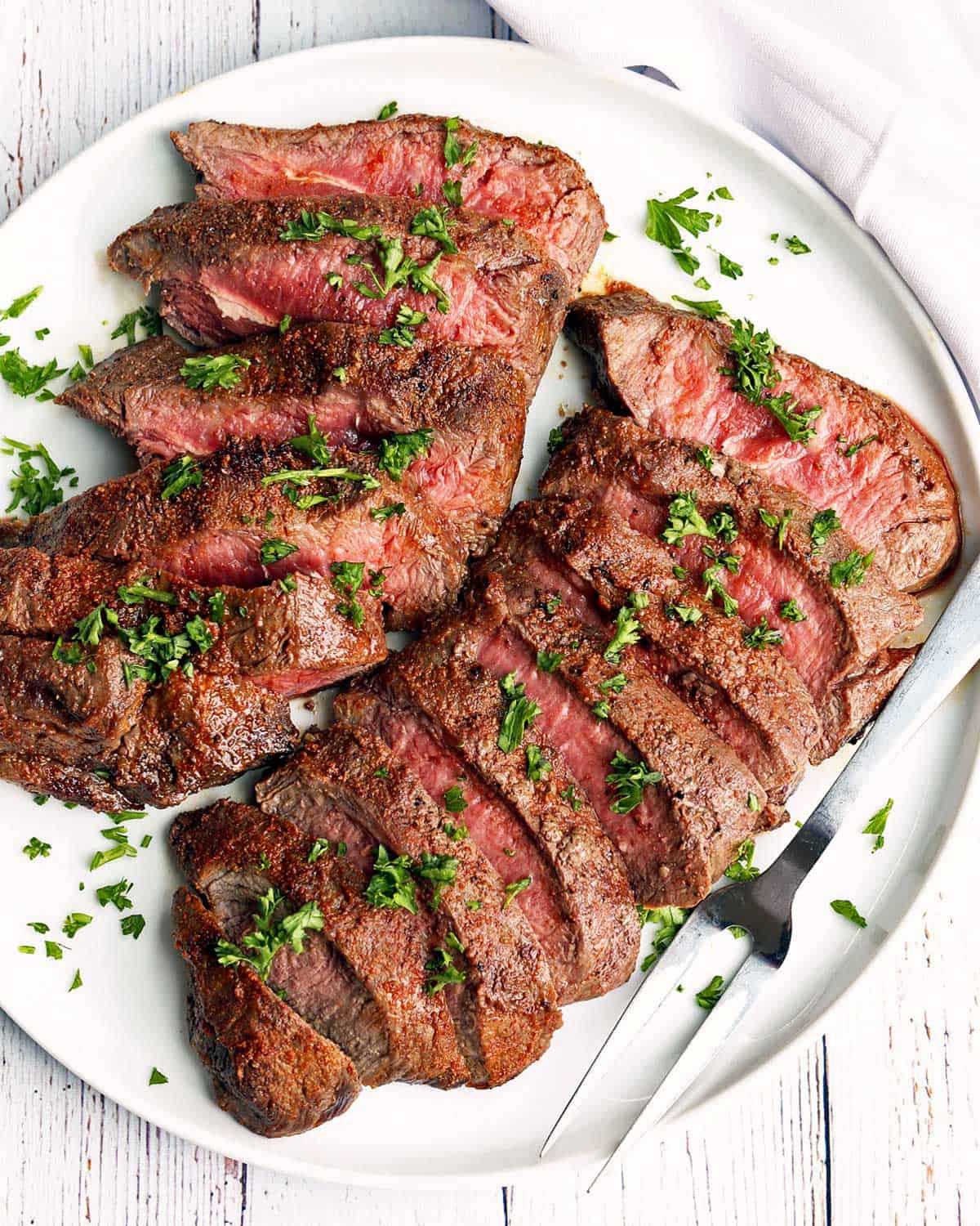 Sliced flat iron steak is served on a white plate.