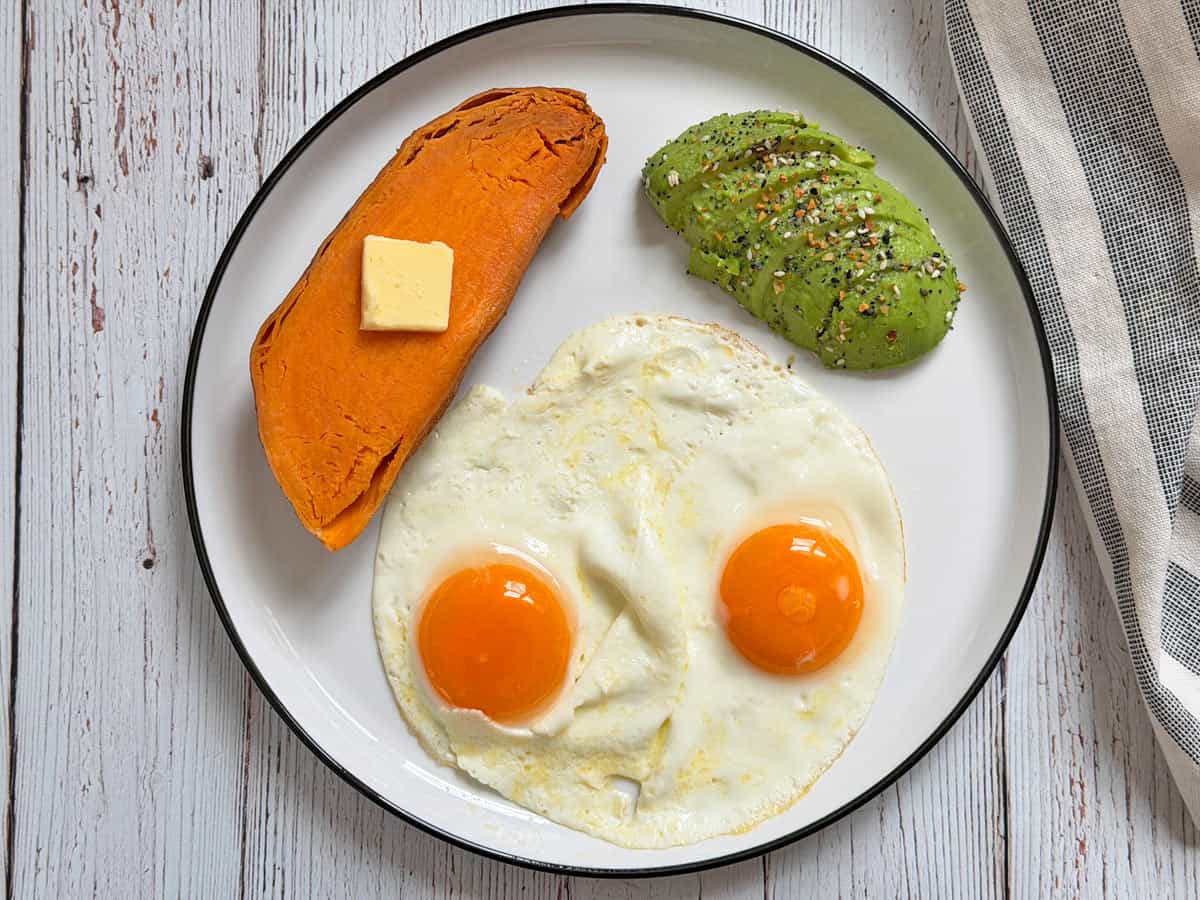 A microwave sweet potato is served for breakfast with eggs and an avocado.
