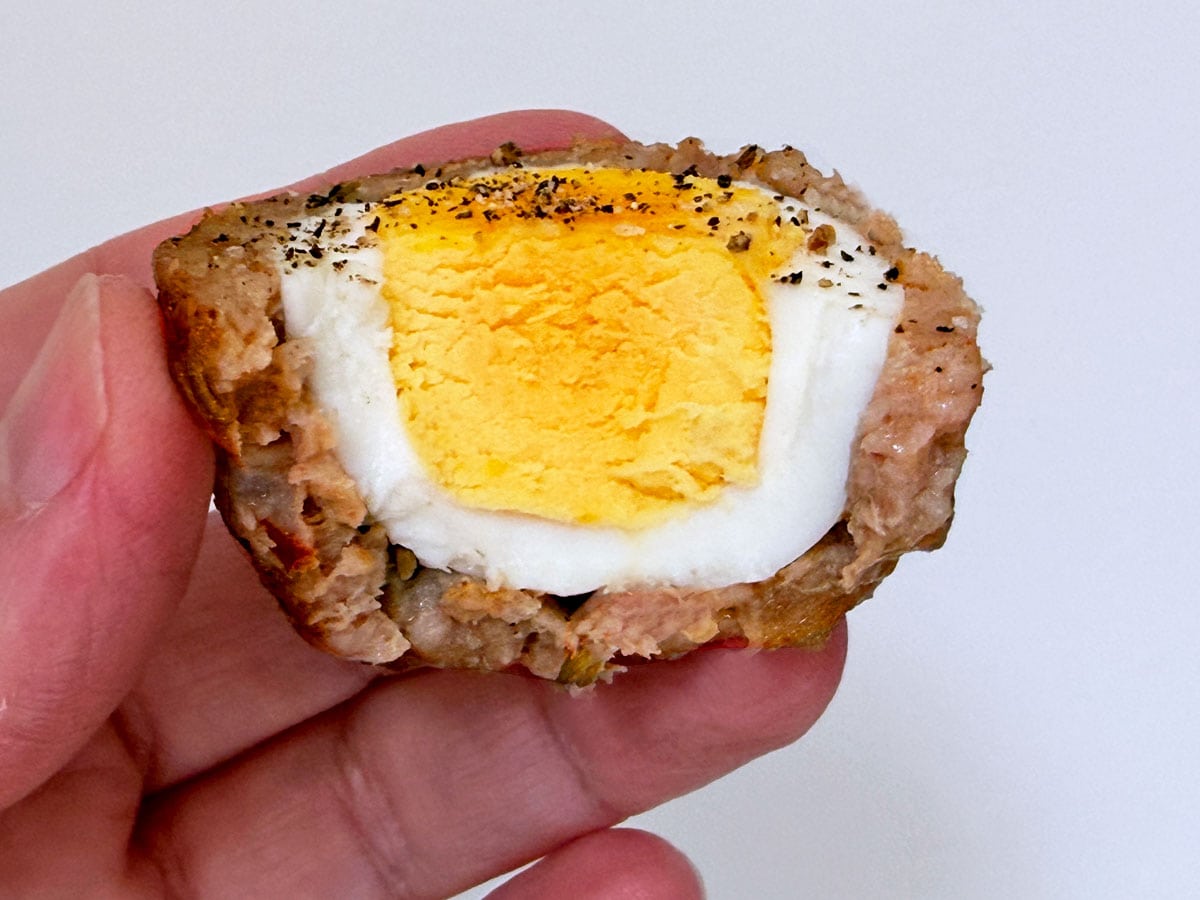 A hand is holding a bitten Scotch egg.