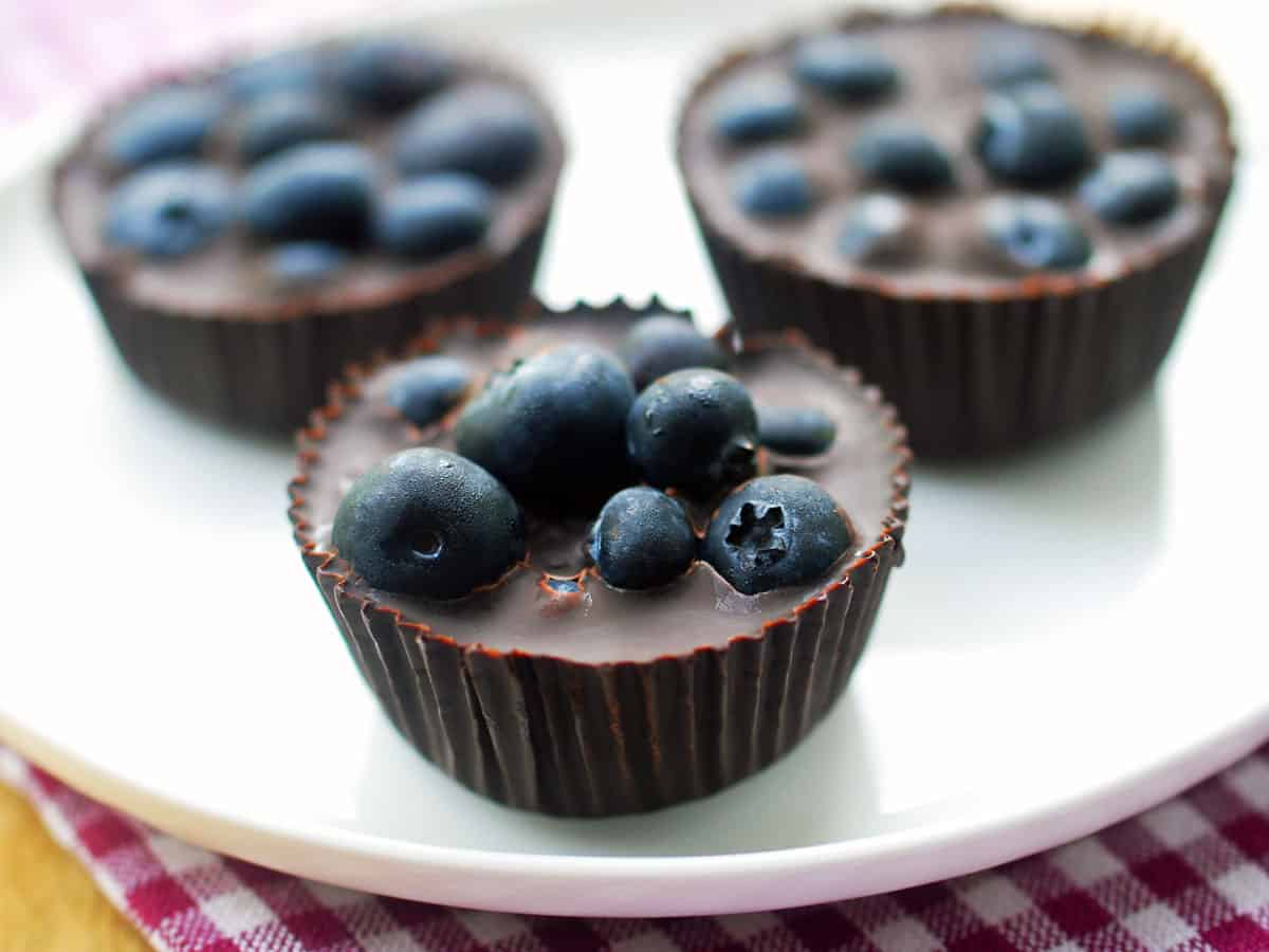 Three chocolate blueberry cups are served on a white plate.