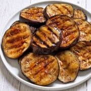 Grilled eggplant is served on a white plate.