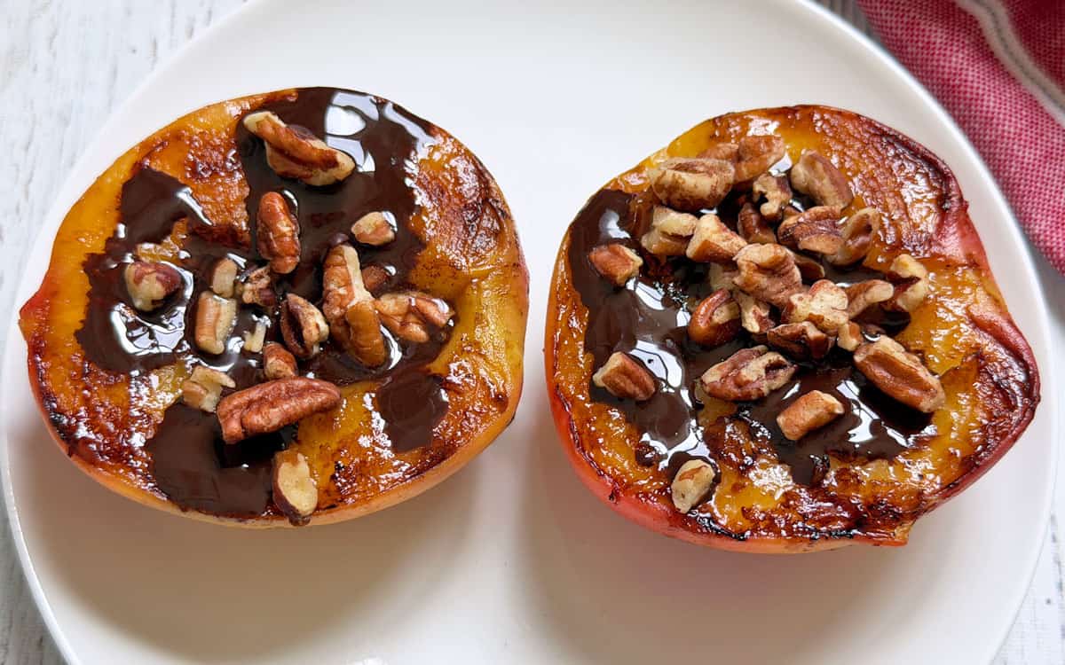 Grilled peaches are topped with chocolate sauce and chopped pecans.