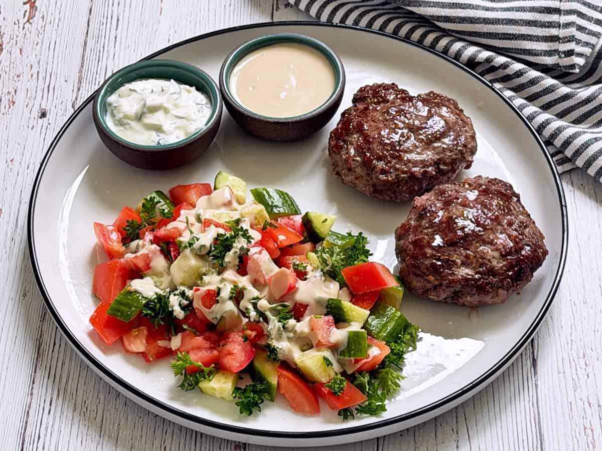 Israeli salad is drizzled with tahini and served with lamb burgers.