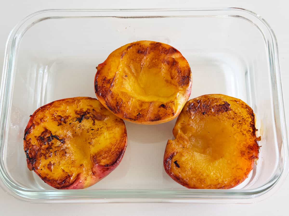 Grilled peaches are stored in a glass container.