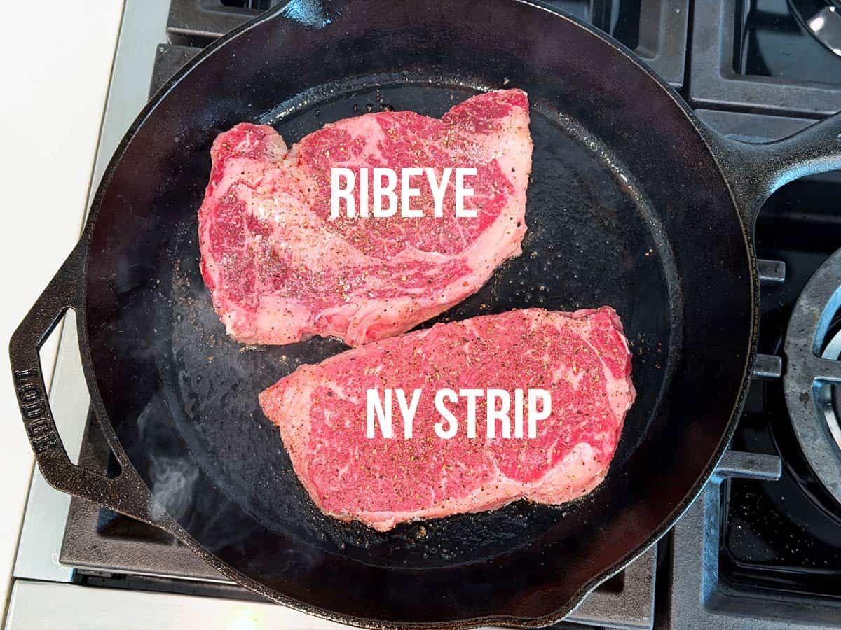 A ribeye steak and a New York Strip steak in a cast-iron skillet.