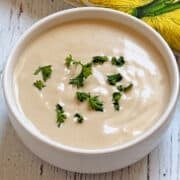 Tahini sauce is served in a white bowl, topped with parsley.