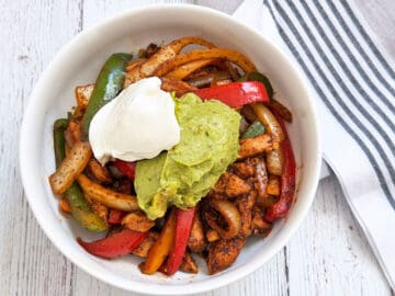 Chicken fajitas are served in a bowl and topped with sour cream and guacamole.