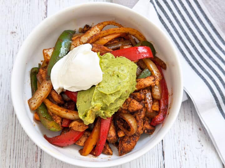 Chicken fajitas are served in a bowl and topped with sour cream and guacamole.