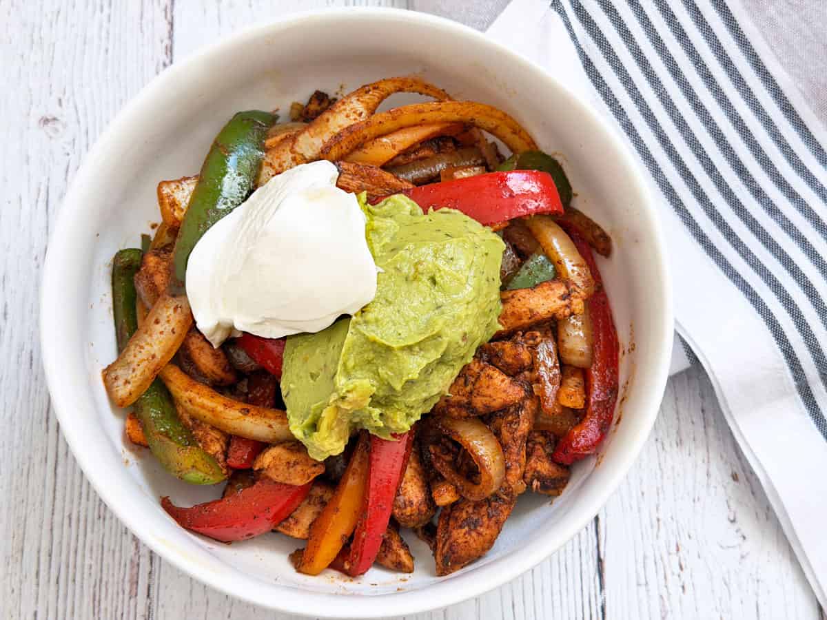 Chicken fajitas are served in a bowl and topped with sour cream and guacamole.