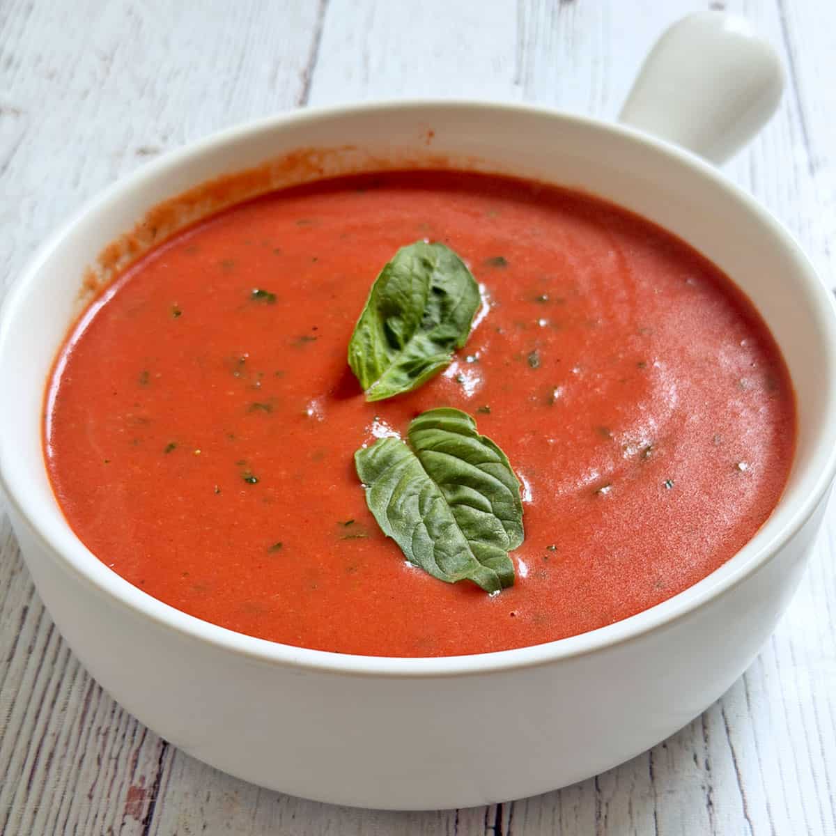 Cold tomato soup is served in a white bowl.