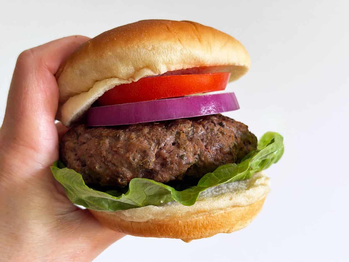 A hand holds a grilled burger in a bun.