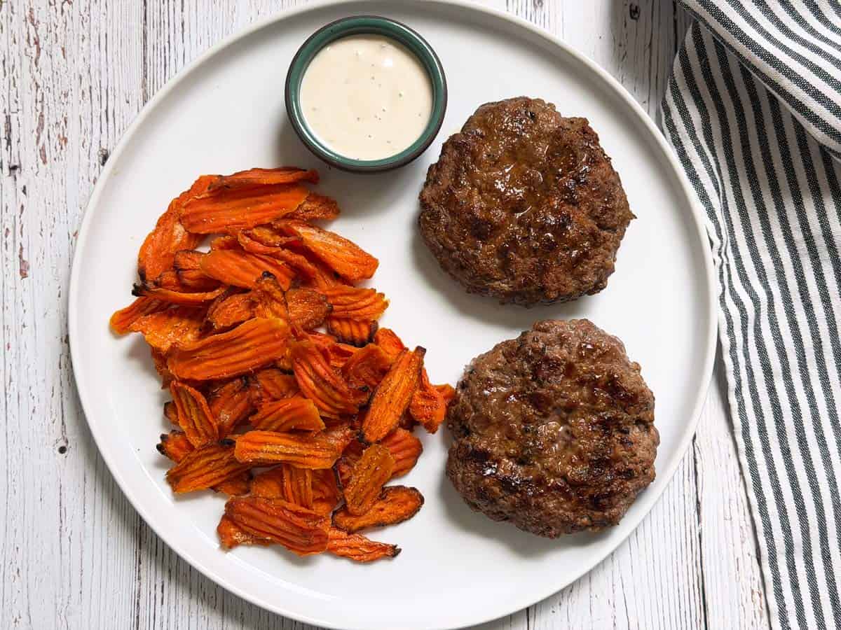 Grilled burgers are served with carrot chips and ranch dressing.
