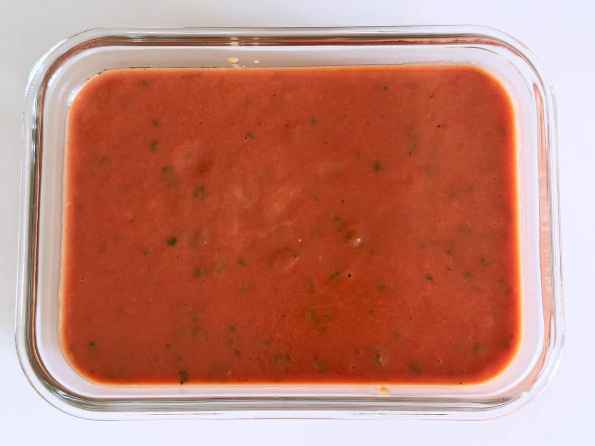 Chilled tomato soup is stored in a glass container.