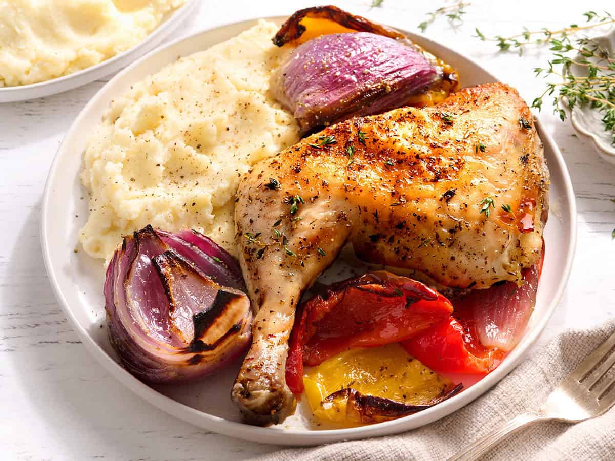 Sheet pan chicken is served on a plate with vegetables and mashed cauliflower.