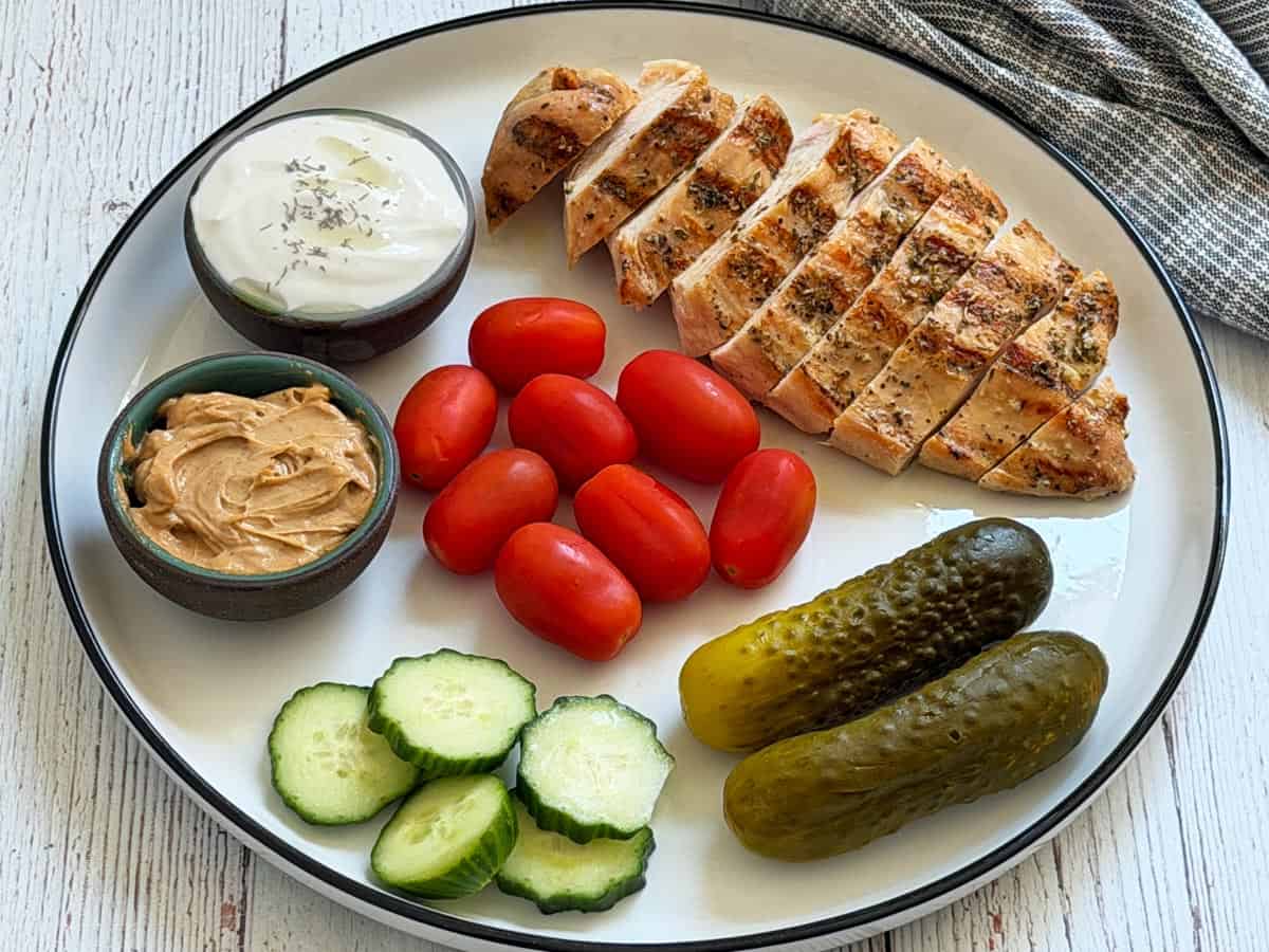 Greek chicken leftovers are served with veggies, pickles, and dips.