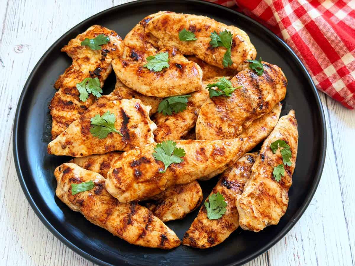 Grilled chicken tenders on a black plate.