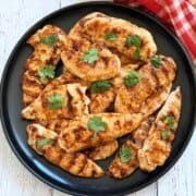 Grilled chicken tenders are served on a black plate garnished with cilantro.