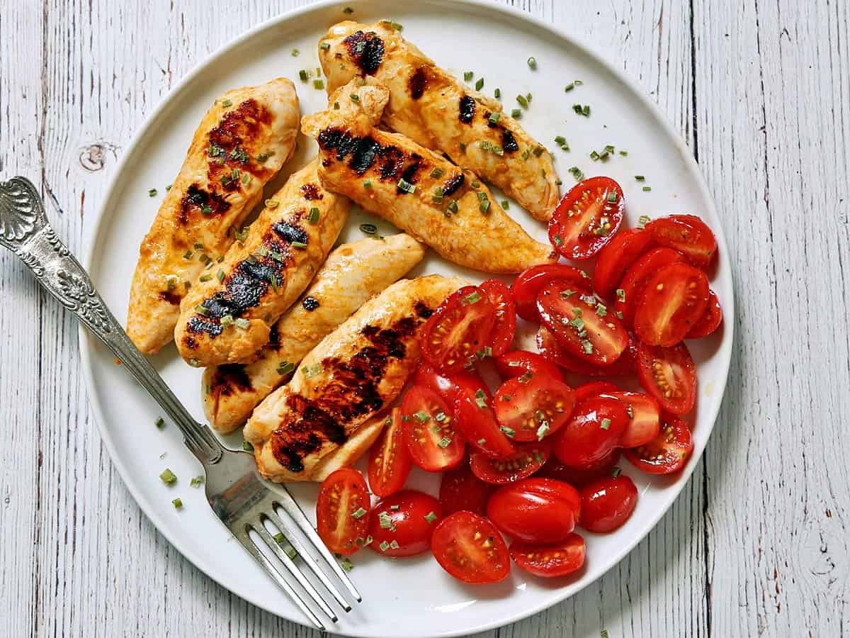 Grilled chicken tenders are served with a tomato salad.