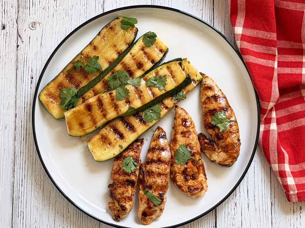 Grilled chicken tenders are served with grilled zucchini.