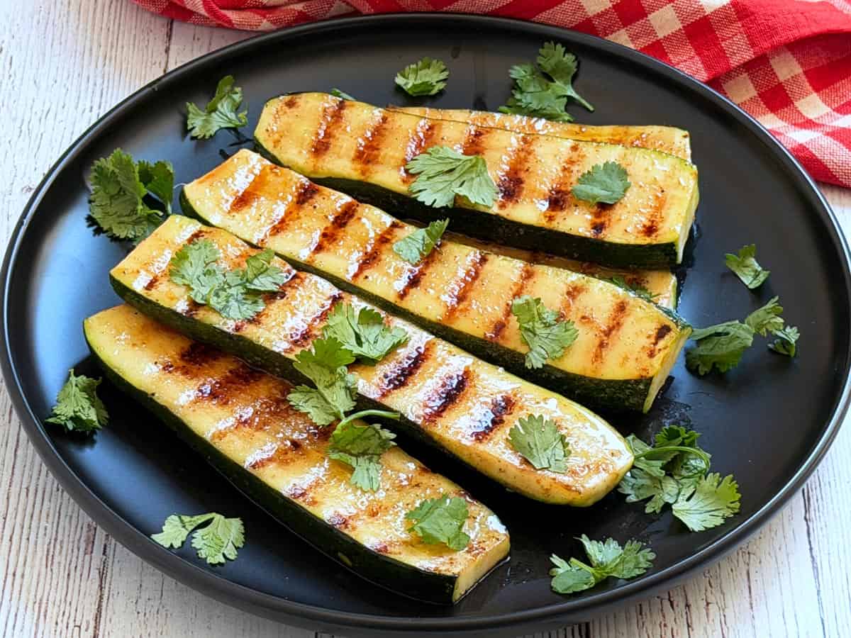 Grilled zucchini is served on a black plate.