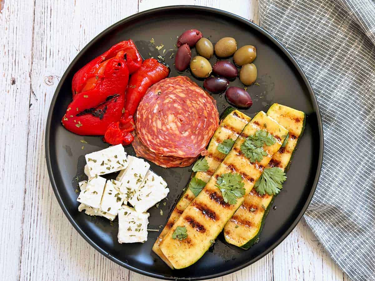 An antipasti plate with grilled zucchini, peppers, olives, feta, and salami.